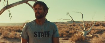 Movie still from “Run & Gun” (2022), directed by Christopher Borrelli – A man standing in the middle of the desert; Medium shot, Over the shoulder angle
