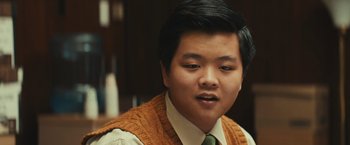 Movie still from “Run & Gun” (2022), directed by Christopher Borrelli – A young man wearing a sweater vest and a tie; Close Up shot, Over the shoulder angle