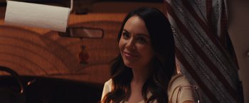 Movie still from “Run & Gun” (2022), directed by Christopher Borrelli – A woman smiles while standing next to a car; Close Up shot, Over the shoulder angle