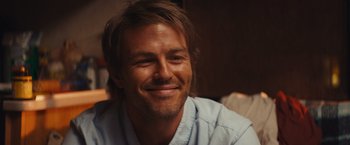 Movie still from “Run & Gun” (2022), directed by Christopher Borrelli – A person smiling for the camera; Close Up shot, Over the shoulder angle