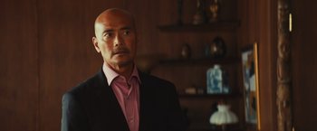 Movie still from “Run & Gun” (2022), directed by Christopher Borrelli – A man in a pink shirt and a black suit; Close Up shot, Over the shoulder angle