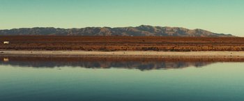 Movie still from “Run & Gun” (2022), directed by Christopher Borrelli – A body of water with a mountain range in the background; Extreme Wide shot, High angle