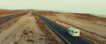 Movie still from “Run & Gun” (2022), directed by Christopher Borrelli – An rv driving down the middle of a road; Extreme Wide shot, High angle