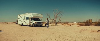 Movie still from “Run & Gun” (2022), directed by Christopher Borrelli – A man standing in front of an rv in the desert; Extreme Wide shot, Low angle