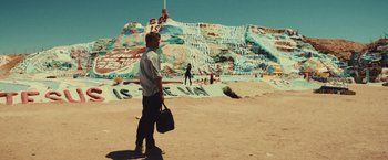 Movie still from “Run & Gun” (2022), directed by Christopher Borrelli – A man standing in front of a mountain covered in graffiti; Wide shot, Low angle