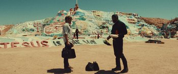 Movie still from “Run & Gun” (2022), directed by Christopher Borrelli – Two men standing in front of a wall covered in graffiti; Wide shot, Over the shoulder angle