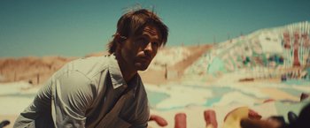 Movie still from “Run & Gun” (2022), directed by Christopher Borrelli – A man in a white dress shirt is standing in the sand; Close Up shot, Low angle