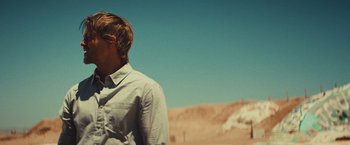 Movie still from “Run & Gun” (2022), directed by Christopher Borrelli – A man standing in the desert looking at the sky; Medium shot, Over the shoulder angle