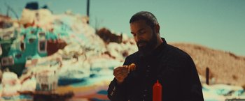 Movie still from “Run & Gun” (2022), directed by Christopher Borrelli – A man with a beard is eating a hot dog; Close Up shot, Over the shoulder angle