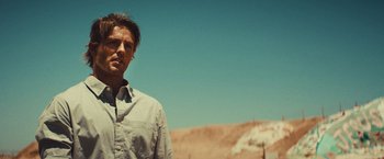 Movie still from “Run & Gun” (2022), directed by Christopher Borrelli – A man standing in the middle of the desert; Close Up shot, Low angle