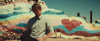 Movie still from “Run & Gun” (2022), directed by Christopher Borrelli – A man standing in front of a colorful rock formation; Medium shot, Over the shoulder angle