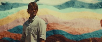 Movie still from “Run & Gun” (2022), directed by Christopher Borrelli – A man standing in front of a colorful wall; Close Up shot, Low angle