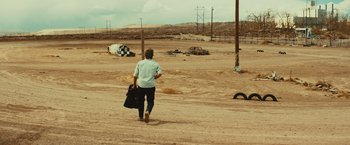 Movie still from “Run & Gun” (2022), directed by Christopher Borrelli – A man walking across a dirt field carrying a bag; Extreme Wide shot, High angle