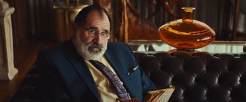 Movie still from “Run & Gun” (2022), directed by Christopher Borrelli – An older man sitting on a couch with a book; Close Up shot, Over the shoulder angle