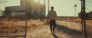 Movie still from “Run & Gun” (2022), directed by Christopher Borrelli – A man walking down a dirt road near a building; Wide shot, Low angle
