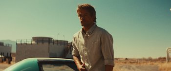 Movie still from “Run & Gun” (2022), directed by Christopher Borrelli – A man standing next to a car on the side of a road; Medium shot, Low angle