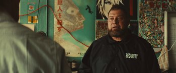 Movie still from “Run & Gun” (2022), directed by Christopher Borrelli – A man standing in front of a wall with a painting on it; Close Up shot, Over the shoulder angle