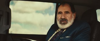 Movie still from “Run & Gun” (2022), directed by Christopher Borrelli – An older man sitting in the driver's seat of a car; Close Up shot, Low angle
