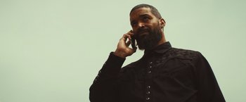 Movie still from “Run & Gun” (2022), directed by Christopher Borrelli – A man with a beard is talking on a cell phone; Close Up shot, Low angle