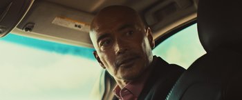 Movie still from “Run & Gun” (2022), directed by Christopher Borrelli – A man with a bald head in a car; Close Up shot, Low angle
