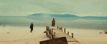 Movie still from “Run & Gun” (2022), directed by Christopher Borrelli – A man standing on a pier on the beach; Extreme Wide shot, Low angle