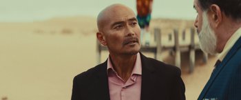 Movie still from “Run & Gun” (2022), directed by Christopher Borrelli – A man in a pink shirt and a black jacket; Close Up shot, Over the shoulder angle