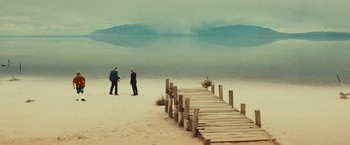 Movie still from “Run & Gun” (2022), directed by Christopher Borrelli – Two men standing on the beach near a wooden pier; Extreme Wide shot, High angle