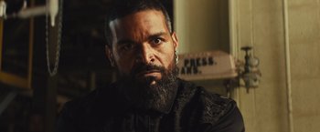 Movie still from “Run & Gun” (2022), directed by Christopher Borrelli – A man with a long beard and a black shirt; Close Up shot, Low angle