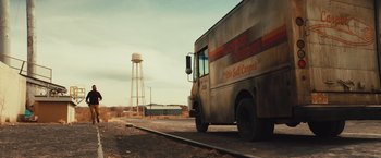 Movie still from “Run & Gun” (2022), directed by Christopher Borrelli – A truck parked on the side of the road near a water tower; Extreme Wide shot, Low angle