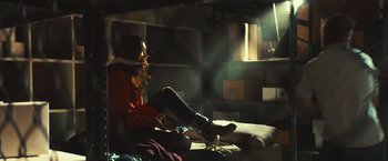 Movie still from “Run & Gun” (2022), directed by Christopher Borrelli – A woman sitting on a bed in a room; Wide shot, Low angle