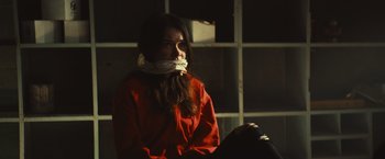 Movie still from “Run & Gun” (2022), directed by Christopher Borrelli – A woman sitting down with her mouth taped shut; Medium shot, Over the shoulder angle