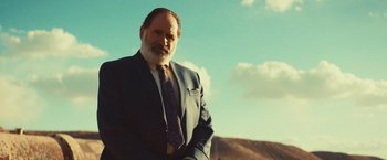 Movie still from “Run & Gun” (2022), directed by Christopher Borrelli – A man in a suit and tie standing in front of a mountain; Medium shot, Low angle