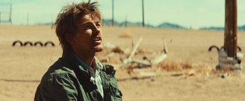 Movie still from “Run & Gun” (2022), directed by Christopher Borrelli – A man standing in the middle of the desert looking up; Close Up shot, Low angle