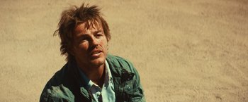 Movie still from “Run & Gun” (2022), directed by Christopher Borrelli – A person sitting on the ground near a wall; Close Up shot, Low angle