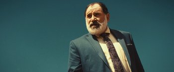 Movie still from “Run & Gun” (2022), directed by Christopher Borrelli – An older man in a suit and a tie; Close Up shot, Low angle
