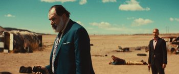 Movie still from “Run & Gun” (2022), directed by Christopher Borrelli – A man in a suit and tie standing in the desert; Medium shot, Over the shoulder angle