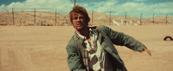 Movie still from “Run & Gun” (2022), directed by Christopher Borrelli – A man in a jacket is standing in the dirt; Medium shot, Over the shoulder angle