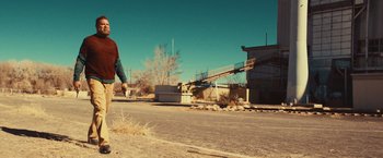 Movie still from “Run & Gun” (2022), directed by Christopher Borrelli – A man riding a skate board down the side of a road; Wide shot, Low angle