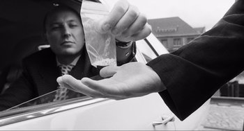 Movie still from “Run Lola Run” (1998), directed by Tom Tykwer – A man in a suit and tie handing a bag of cocaine out of a car window; Close Up shot, Low angle