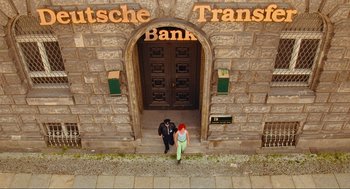 Movie still from “Run Lola Run” (1998), directed by Tom Tykwer – A man and a woman standing in front of a bank; Wide shot, Overhead angle