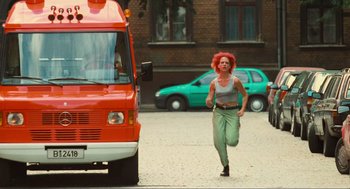Movie still from “Run Lola Run” (1998), directed by Tom Tykwer – A woman running in front of an orange van; Wide shot, High angle