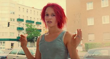Movie still from “Run Lola Run” (1998), directed by Tom Tykwer – A woman with red hair is standing in the street; Medium shot, Low angle