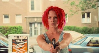 Movie still from “Run Lola Run” (1998), directed by Tom Tykwer – A woman with red hair is holding a gun; Medium shot, Low angle