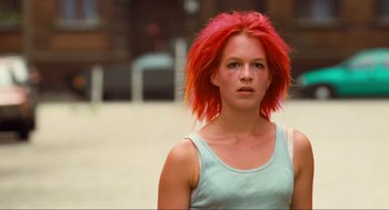 Movie still from “Run Lola Run” (1998), directed by Tom Tykwer – A woman with red hair is standing in the street; Close Up shot, Low angle