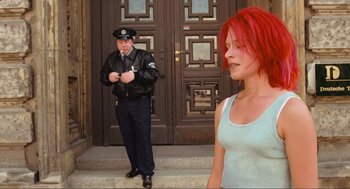 Movie still from “Run Lola Run” (1998), directed by Tom Tykwer – A police officer standing next to a woman in front of a building; Medium shot, Low angle