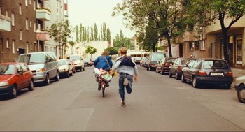 Movie still from “Run Lola Run” (1998), directed by Tom Tykwer – Two people riding a bike down a street; Wide shot, Over the shoulder angle