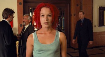 Movie still from “Run Lola Run” (1998), directed by Tom Tykwer – A woman with red hair is standing in front of two men; Medium shot, Over the shoulder angle