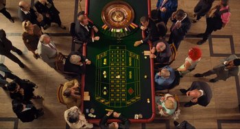 Movie still from “Run Lola Run” (1998), directed by Tom Tykwer – A group of people sitting around a table with roulette; Wide shot, Overhead angle