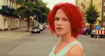 Movie still from “Run Lola Run” (1998), directed by Tom Tykwer – A woman with red hair standing on the side of the street; Close Up shot, Low angle