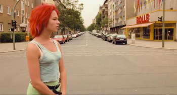 Movie still from “Run Lola Run” (1998), directed by Tom Tykwer – A woman with red hair standing on the side of a street; Medium shot, Over the shoulder angle